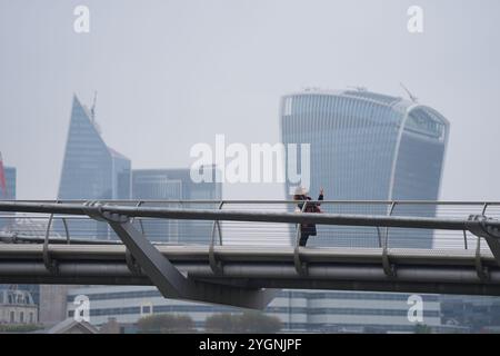 Eine Frau hält an, um ein Foto auf der Millennium Bridge in London zu machen, da der Himmel grau wird, weil der Druck über Großbritannien Feuchtigkeit in der Nähe der Erdoberfläche einschließt, wodurch hartnäckige Wolken oder, im Wetterverständnis, „antizyklische Dunkelheit“ entstehen. Hoher Druck führt zu wenig oder gar keinem Wind, der die Wolke sonst umherbewegen und aufbrechen würde. Bilddatum: Freitag, 8. November 2024. Stockfoto