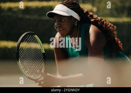 Afroamerikanische Frau in Aktion, die im Freien Tennis spielt, Fokus und Leichtathletik zeigt. Sie hat lange lockige Haare und genießt den Sport in der Sonne Stockfoto