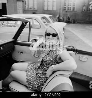 Junge blonde Frau mit Sonnenbrille sitzt in einem Cabrio in der Innenstadt von Ost Berlin, DDR 1968. Stockfoto