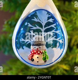 Tropfenförmige weihnachtsdekoration, die einen Miniatur-Schneemann mit einem rot-weißen Schal und eine Winterszene mit einem verschneiten Baum umschließt Stockfoto