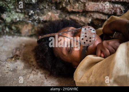 Porträt einer schwarzen Frau, gekettet und mit einer eisernen Maske über dem Mund, die auf dem Boden liegt. Sklaverei in Brasilien. Darstellung der Sklavin Anastacia. Stockfoto