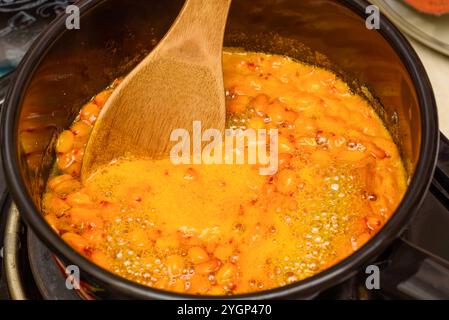 Die kochenden Sanddornbeeren mit Zucker in einem Topf mit einem Holzlöffel rühren. Papierstau. Stockfoto