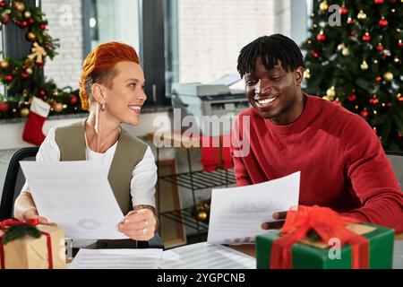 Kollegen teilen Lachen und feierlichen Beifall, während sie während einer Feiertagsfeier Geschenke austauschen. Stockfoto