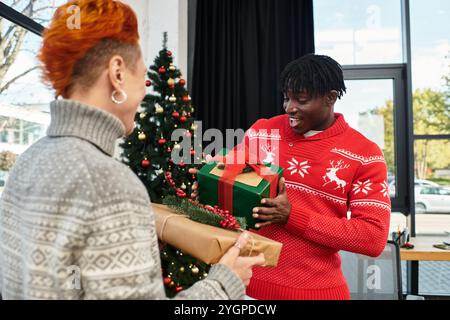 Zwei junge Kollegen teilen einen Moment des Glücks, während sie während der Weihnachtszeit Geschenke austauschen Stockfoto