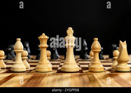 Hölzerne Schachfiguren stehen auf Schachbrett auf schwarzem Hintergrund Stockfoto