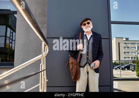 Ein modischer Seniorenmann steht selbstbewusst neben einer eleganten Struktur und zeigt sein herbstliches Outfit mit Charme. Stockfoto