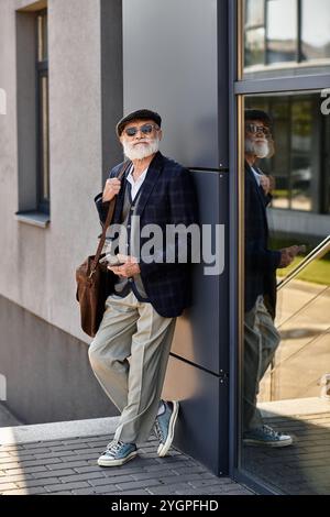 Ein modischer Seniorenmann steht im Herbst souverän an einem eleganten Gebäude und zeigt seinen eleganten, legeren Stil. Stockfoto