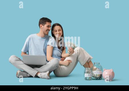 Junges Paar mit Geld, das Laptop auf blauem Hintergrund benutzt Stockfoto