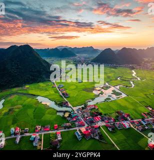 Aus der Vogelperspektive auf den Sonnenuntergang über dem Bac Son Valley mit Bergen, üppigen Reisfeldern mit gewundenen Fluss und traditionellem Dorf auf dem Land in lang Son, V Stockfoto