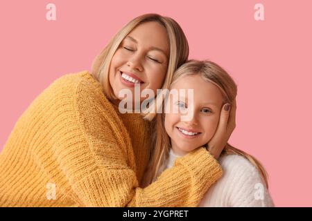 Schöne Frau und ihre süße Tochter in stylischen Pullis auf rosa Hintergrund Stockfoto