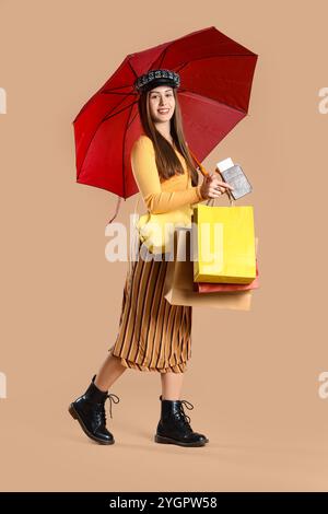 Weibliche Touristen in Herbstkleidung mit Regenschirm, Reisepass und Taschen auf beigefarbenem Hintergrund Stockfoto