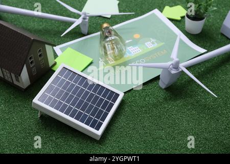 Sonnenkollektor mit Windturbinen und Glühbirne auf Gras, Nahaufnahme. Konzept der grünen Energie Stockfoto