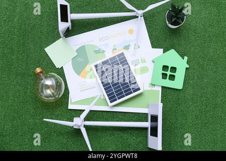 Windturbinen mit Hausfigur, Solarmodul und Glühbirne auf Gras. Konzept der grünen Energie Stockfoto