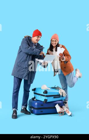 Nettes junges Paar mit Laptop, Koffern und Tickets auf blauem Hintergrund. Winterurlaubskonzept Stockfoto