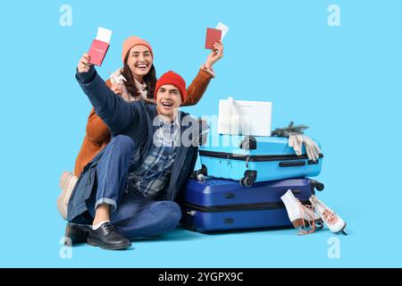 Nettes junges Paar mit Laptop, Koffern, Pässen und Reiseaccessoires auf blauem Hintergrund. Winterurlaubskonzept Stockfoto