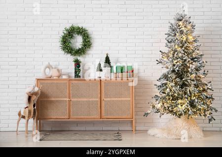 Kommode mit Dekor, Weihnachtsbaum, Rentier aus Holz und Mistelkranz an weißer Backsteinwand im Zimmer Stockfoto