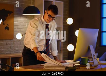 Junger Geschäftsmann, der nachts im Büro mit Papieren arbeitet Stockfoto