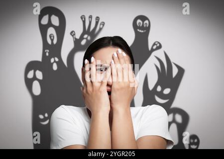 Frau, die von Monstern erschreckt wird. Gruselige Schatten auf der weißen Wand Stockfoto