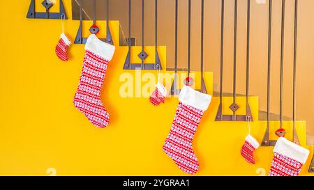 Ein festliches Arrangement gestrickter Weihnachtsstrümpfe hängt an einem modernen Treppengeländer mit gelber Wand. Stockfoto