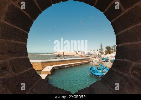 Historischer Hafen von Essaouira, Marokko, mit blauen Fischerbooten, die neben berühmten alten Festungsmauern anlegen und den Charme der Küste und das maritime HE einfangen Stockfoto