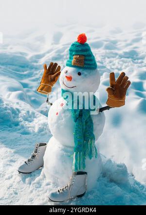 Lustiger Schneemann in stylischem Hut und Schal auf verschneiten Feldern. Schneemann der Freund steht im Winterhut und Schal mit roter Nase. Niedlicher Schneemann bei einem Schnee Stockfoto