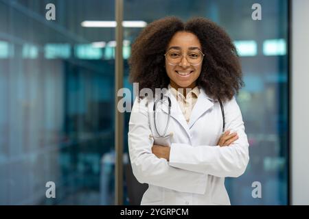 Selbstbewusste afroamerikanische Ärztin mit weißem Labormantel, stehend mit gefalteten Armen im Krankenhaus. Medizinischer Fachmann mit Sicherheit und Expertise im Gesundheitswesen. Stockfoto