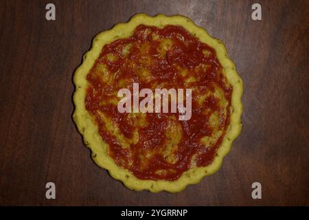 Glutenfreie Pizzakruste mit Pizzasauce auf einem Holztisch, Speisenvorbereitung, Vorbereitung zum Abendessen, Zöliakie-Krankheit, Glutenalternative, Molkereifrei Stockfoto