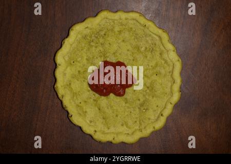 Glutenfreie Pizzakruste mit Pizzasauce auf einem Holztisch, Speisenvorbereitung, Vorbereitung zum Abendessen, Zöliakie-Krankheit, Glutenalternative, Molkereifrei Stockfoto