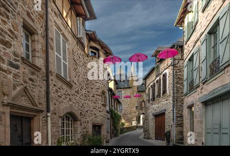 Uzerche, Coreze, Nouvelle-Aquataine, Frankreich - 8. November 2024 - in einer alten französischen Stadt mit pinkfarbenen Sonnenschirmen auf der anderen Straßenseite Stockfoto