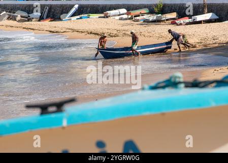 Am Strand von Rio Vermelho werden Fischer gesehen, die ein Fischerboot auf das Meer schieben. Salvador, Bahia. Stockfoto