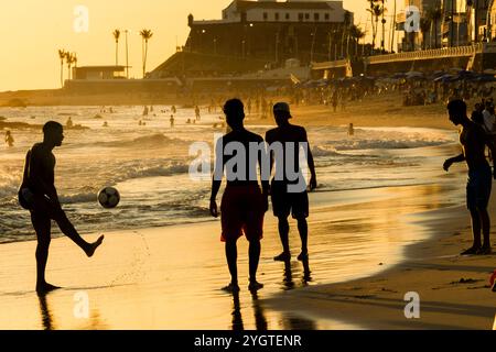 Salvador, Bahia, Brasilien - 6. Dezember 2019: Menschen werden bei Sonnenuntergang am Strand von Farol da Barra in Salvador, Bahia, beim Fußballspielen beobachtet. Stockfoto