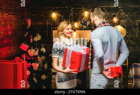 Liebevolles Weihnachtspaar, das die Feiertage und Geschenke genießt. Überraschung für Liebste. Fröhliche Liebhaber tauschen am Weihnachtsabend Geschenkboxen aus. Weihnachten Stockfoto