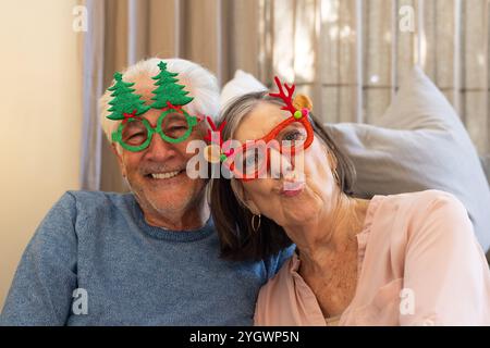 Weihnachten, Selfie machen, Seniorenpaar mit festlicher Brille, lächeln, zu Hause Stockfoto