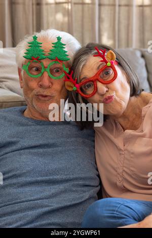 Weihnachten, Selfie machen, Seniorenpaar mit festlicher Brille, lustige Gesichter zu Hause machen Stockfoto