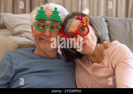 Weihnachten, Selfie machen, ein Paar mit festlicher Brille, lustige Gesichter zu Hause Stockfoto