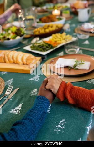 Weihnachtszeit, multirassische Familie hält Hände an festlichem Esstisch, zu Hause Stockfoto