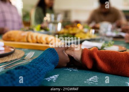 Weihnachtszeit, multirassische Familie hält Hände an Feiertagstisch, zu Hause Stockfoto