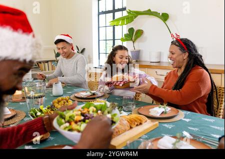 Familie mit mehreren Rassen, die Weihnachten feiert, Essen teilt und lacht am festlichen Dinner-Tisch, zu Hause Stockfoto