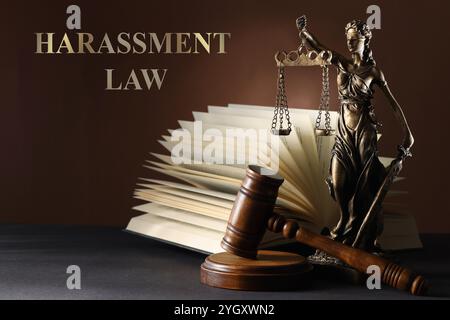 Belästigungsgesetz. Statue von Lady Justice in der Nähe des Hamels und offenes Buch auf grauem Tisch Stockfoto