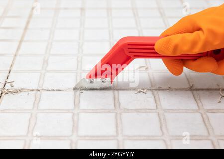 Die Haushälterin entfernt alte Fugen von den Badezimmerfliesen. Ausharken von Fugenfliesen zum Nachfugen. Stockfoto