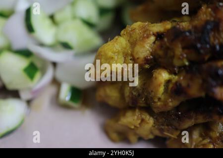 Nahaufnahme von saftigem gegrilltem Hühnersatay auf Spießen neben frischen Gurkenscheiben. Stockfoto