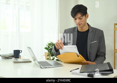 Konzentrierter Geschäftsmann, der wichtige Dokumente am Schreibtisch untersucht Stockfoto