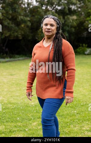 Frau, die im Garten läuft, trägt einen orangefarbenen Pullover und blaue Jeans Stockfoto