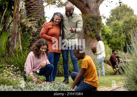 Eine Familie, die eine gemeinsame Rasse hat, genießt Gartenarbeit im Garten, lächelt und sich über Pflanzen zusammenhält Stockfoto