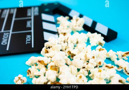 Nahaufnahme einer schwarz-weißen Holzklatschtafel mit Popcorn auf blauem Hintergrund. Horizontales Bild, Kinokonzept und Spaß Stockfoto