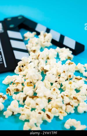 Vertikales Bild einer schwarz-weißen Holzklatschtafel mit Popcorn auf blauem Hintergrund, Konzept des Kinos und Spaß Stockfoto