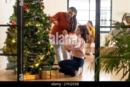 Multirassische Frau und Kind schmücken den weihnachtsbaum für festliche Feiertage zusammen, zu Hause Stockfoto