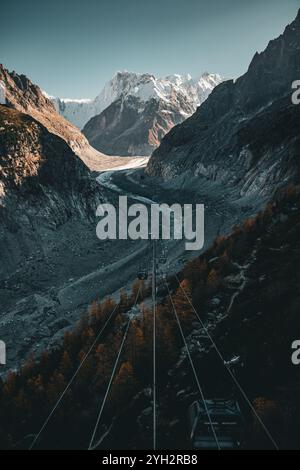 Majestätische Aussicht auf eine Seilbahn zum Mer de Glace, umgeben von hohen Gipfeln und einem sich windenden Gletscher mit lebhaften Herbstbäumen. Stockfoto