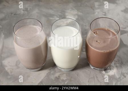 Leckere Proteinshakes in Gläsern auf grauem, strukturiertem Tisch, Nahaufnahme Stockfoto