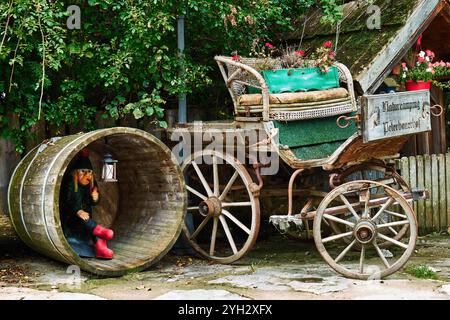 Vintage-Kutsche mit Holzfass und skurrilem Dekor im Garten Stockfoto